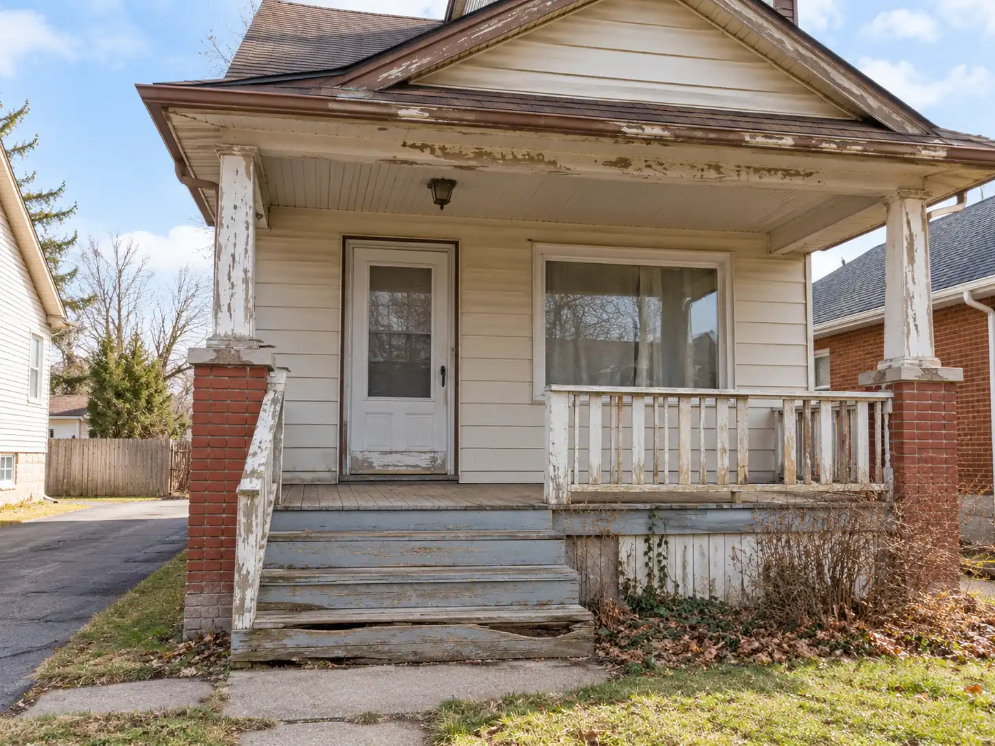 Older home's weathered front porch with peeling paint and damaged wooden steps